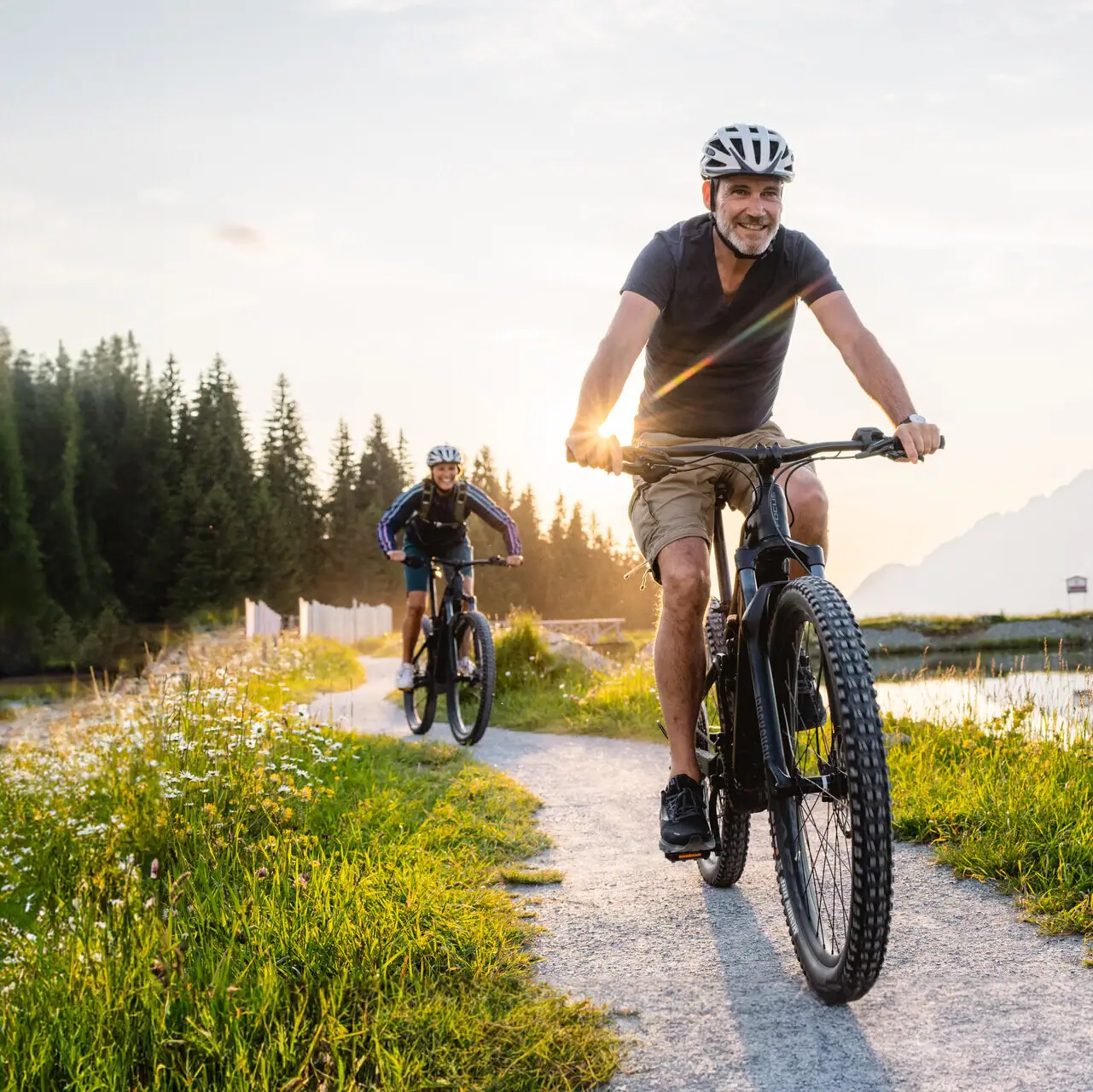 Ein Mann fährt auf einem Fahrrad auf einem Weg mit einem See und Bergen im Hintergrund.