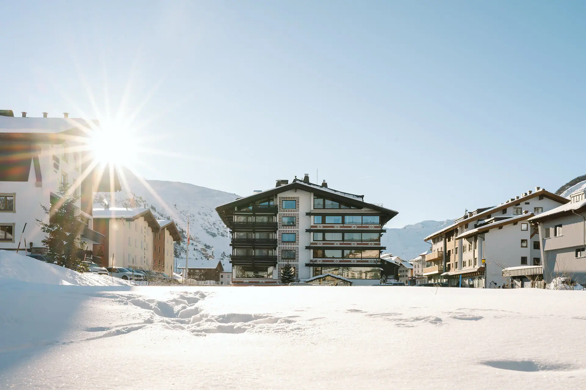 A-ROSA Hotel in Zürs Schneebedeckter Boden mit Gebäuden und Bergen im Hintergrund.