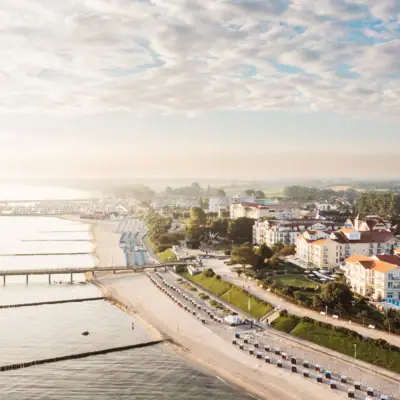 A-ROSA Ostseehotel Kühlungsborn Strand mit Gebäuden und einer Brücke im Hintergrund.