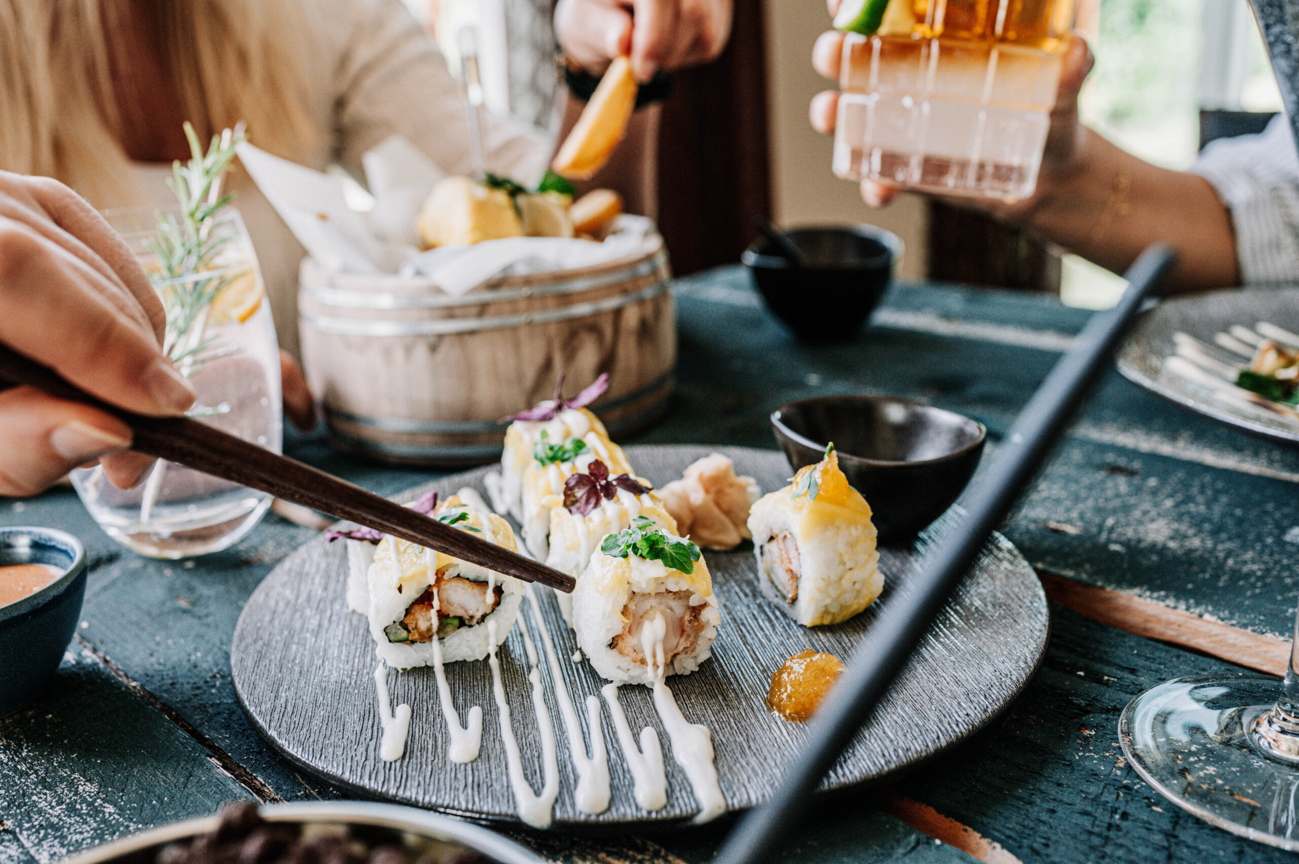 Sieben Sushi-Stücke dekorativ angerichtet auf einer runden Schieferplatte.