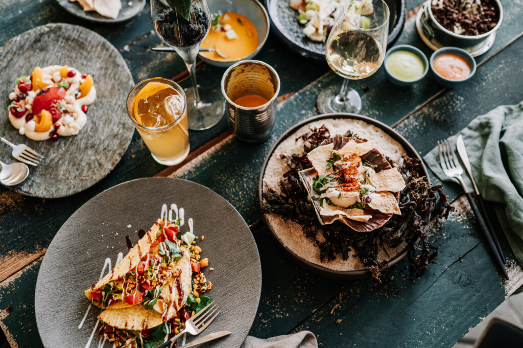 Ceviche aus Kingfish mit Granny Smith und Piment d'espelettes serviert auf einem dunklen Teller mit einem Glas Sprudelwasser mit Orange und Rosmarin.