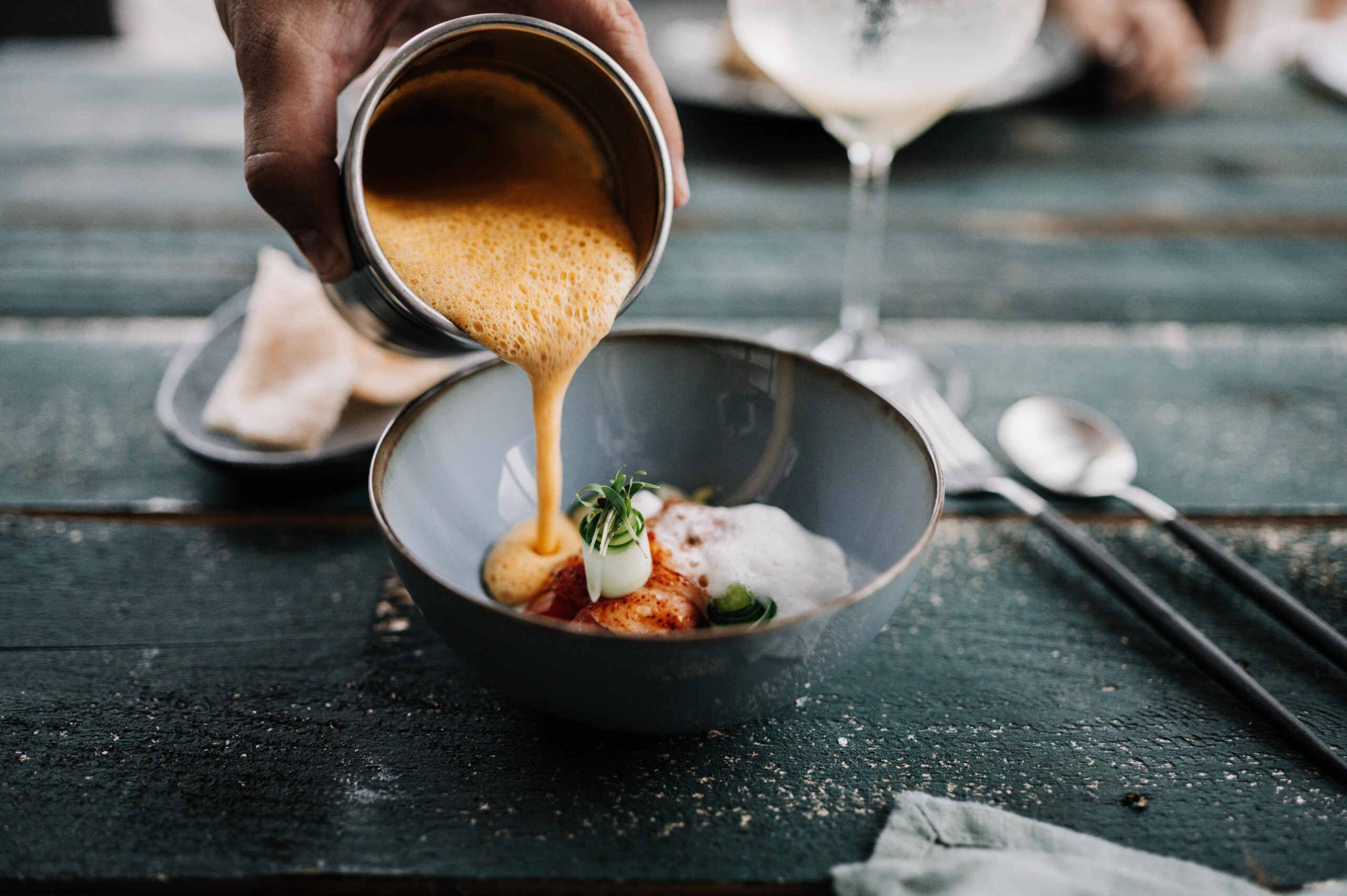 Ein Fischgericht wird in einer Schale durch das Begießen mit einer Schaumsauce verfeinert.