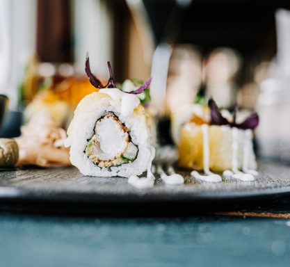 Sushi-Reisröllchen gefüllt mit knusprig gebackenem Hühnchenfleisch und dekoriert mit Kräutern und Mayonnaise.